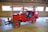 A bright red vintage firefighting vehicle with an open cabin is parked inside a wooden building. The vehicle has large tires and is equipped with firefighting equipment on the front. The wooden interior of the building features several rectangular windows, allowing natural light to illuminate the scene.