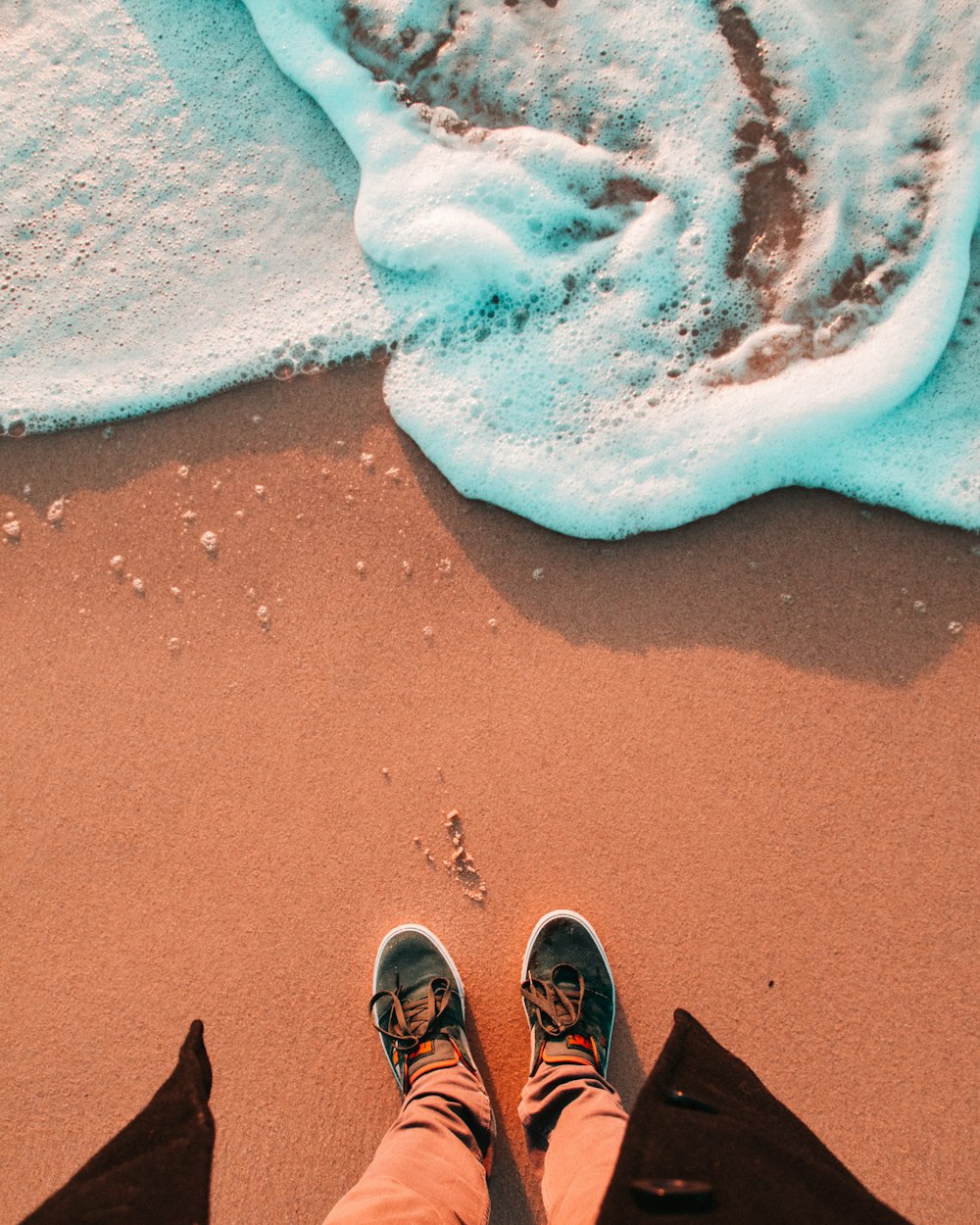 person wearing black shoes standing in front of seashore waves