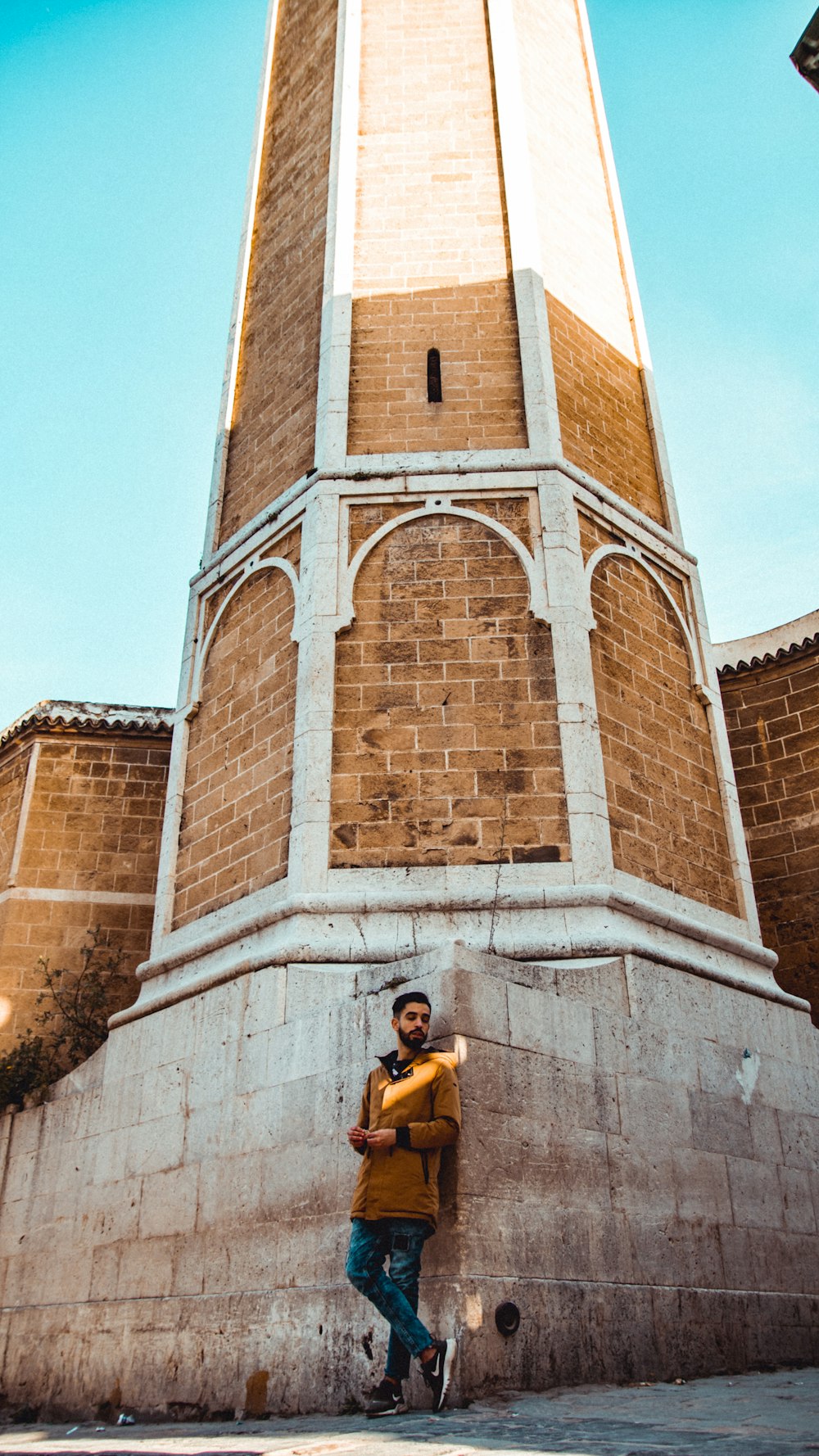 man in brown top leaning on wall during daytime