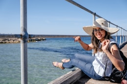 woman sitting below railings near body of water during daytime