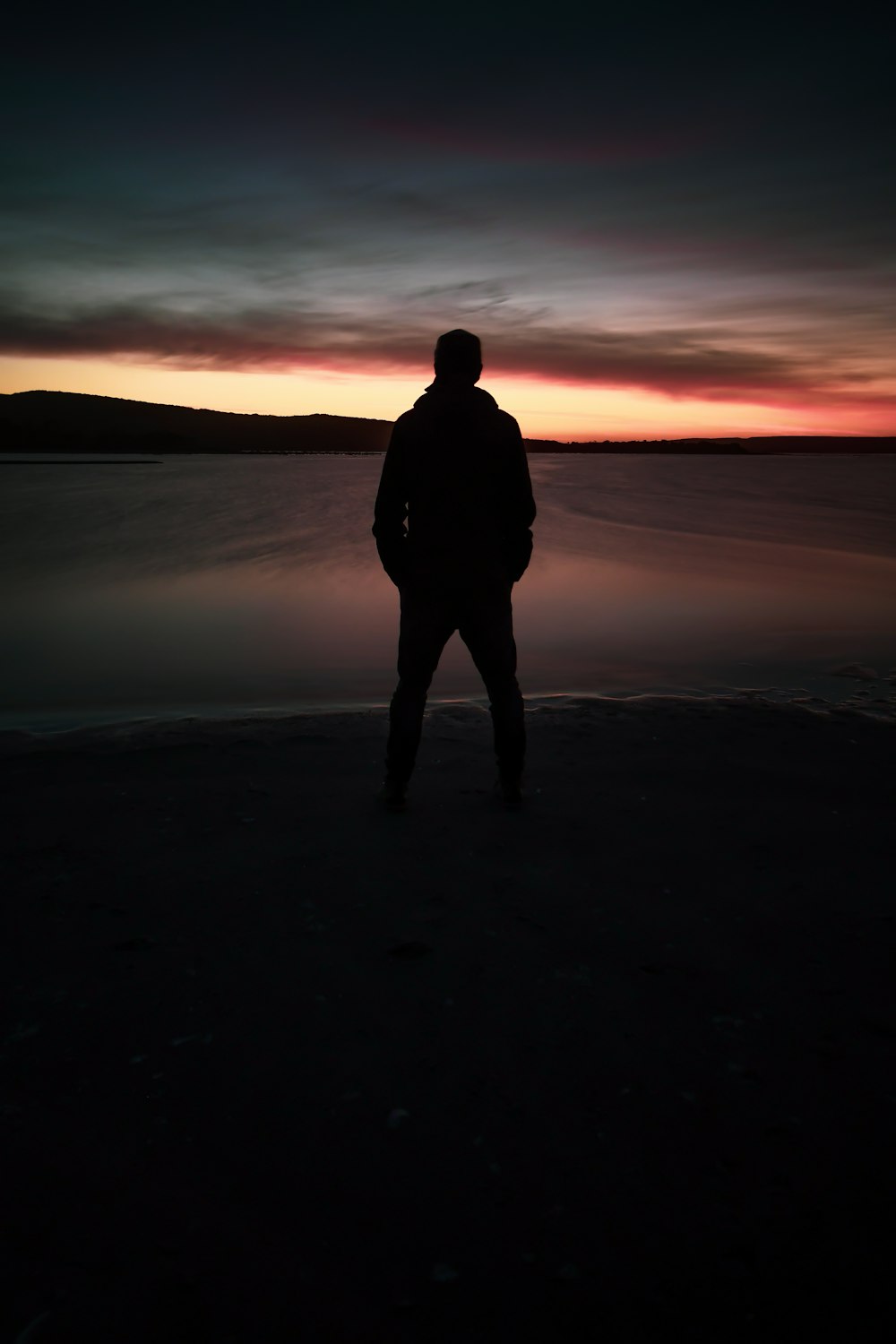 silhouette of person standing and facing on calm sea during golden hour