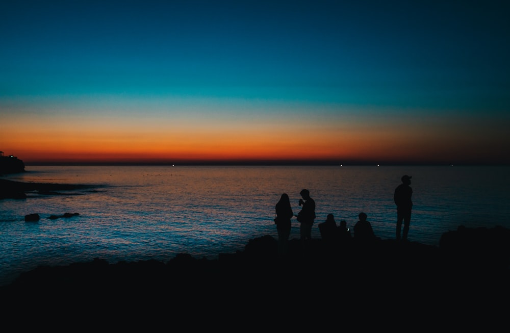 Silhouette von Menschen, die während der goldenen Stunde in der Nähe eines Gewässers stehen