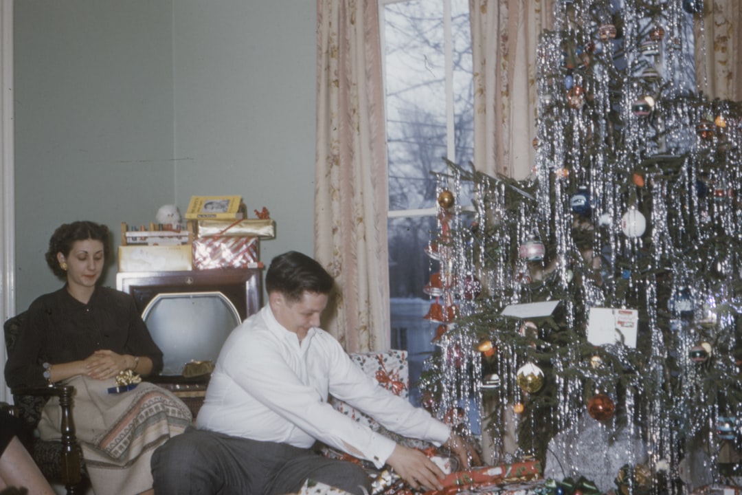 man wearing white shirt sitting near woman and Christmas tree