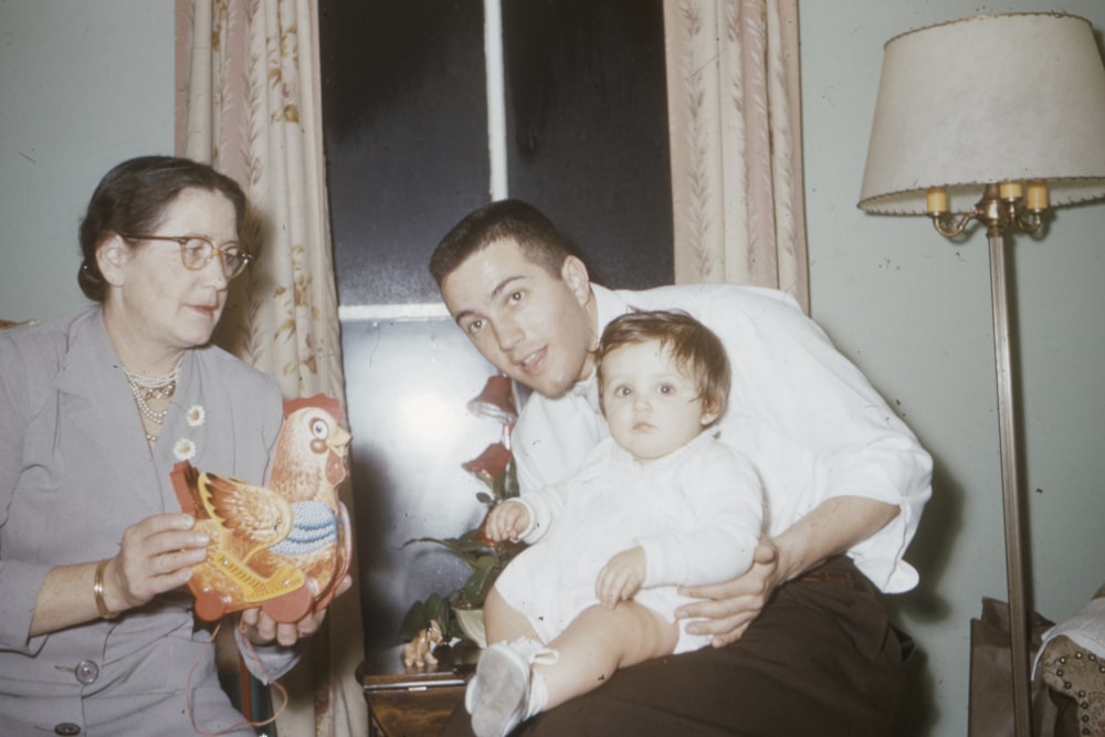 man in white shirt holding baby while sitting near woman inside room