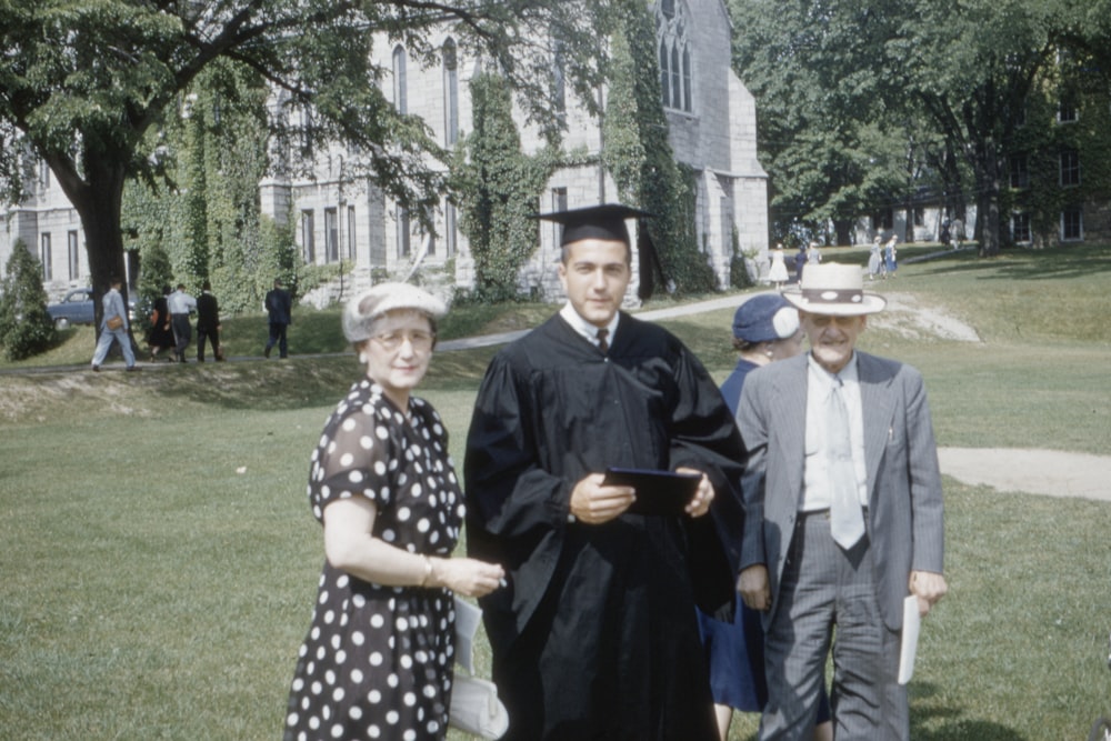 man wearing academic suit standing beside man and woman