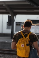 man carrying yellow backpack in train station