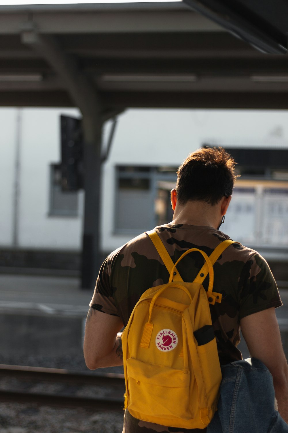 Hombre que lleva una mochila amarilla en la estación de tren