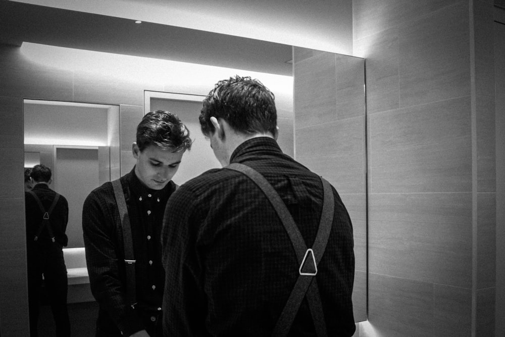 grayscale photography of man standing front of mirror