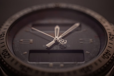 A close-up of a sophisticated wristwatch with a dark dial and luminescent hands. The bezel is marked with numbers, and there is a digital display beneath the hands indicating additional features. The brand name and model are subtly visible on the dial, indicating a premium design.