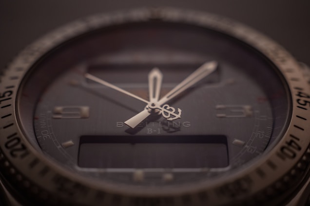 A close-up of a sophisticated wristwatch with a dark dial and luminescent hands. The bezel is marked with numbers, and there is a digital display beneath the hands indicating additional features. The brand name and model are subtly visible on the dial, indicating a premium design.