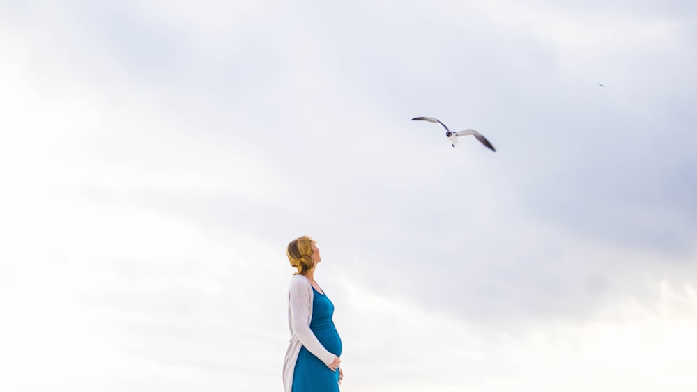 woman in blue and white dress standing and looking at flying bird