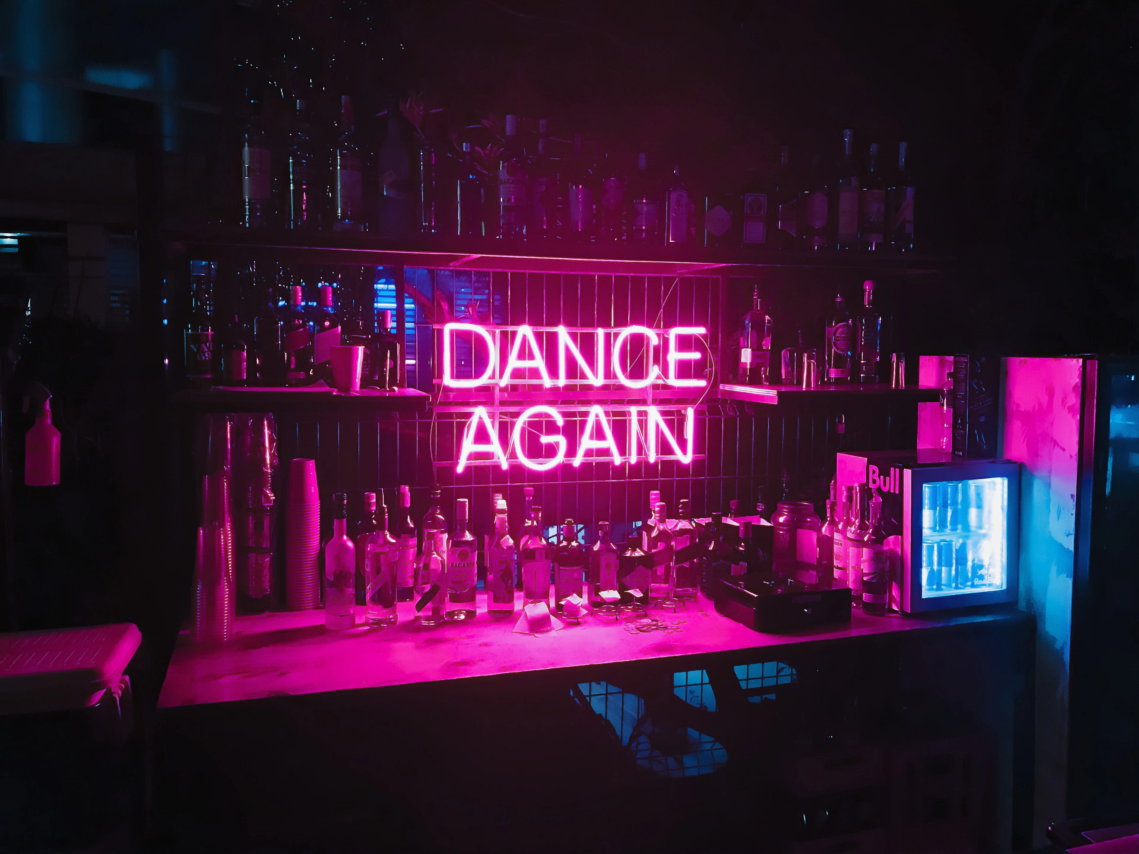 A neon sign reading Dance Again above the bar