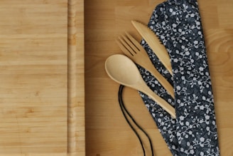 a wooden spoon, fork, and knife rest on a bamboo cutting board