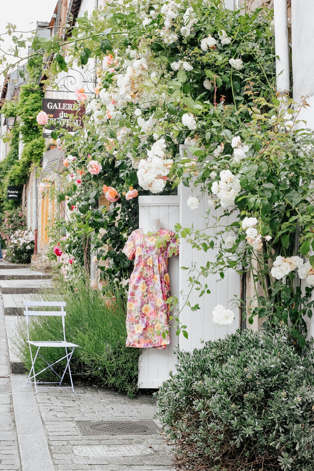 a dress hanging on a white fence next to flowers