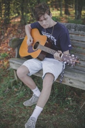 man playing guitar on bench while sitting