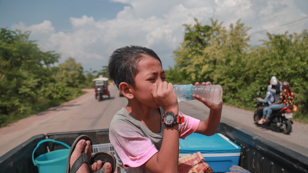 person drinking on bottled water at pickup truck during daytime