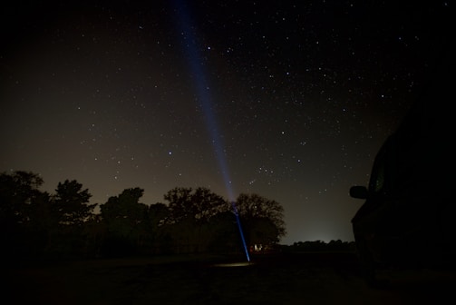 Projector casting light onto a white sheet hung between trees in a rural setting.