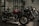 A row of sleek motorcycles is on display in a showroom setting. The motorcycles are primarily black and red, with chrome detailing, and are lined up side by side. The room is dimly lit, creating a dramatic and sophisticated atmosphere.