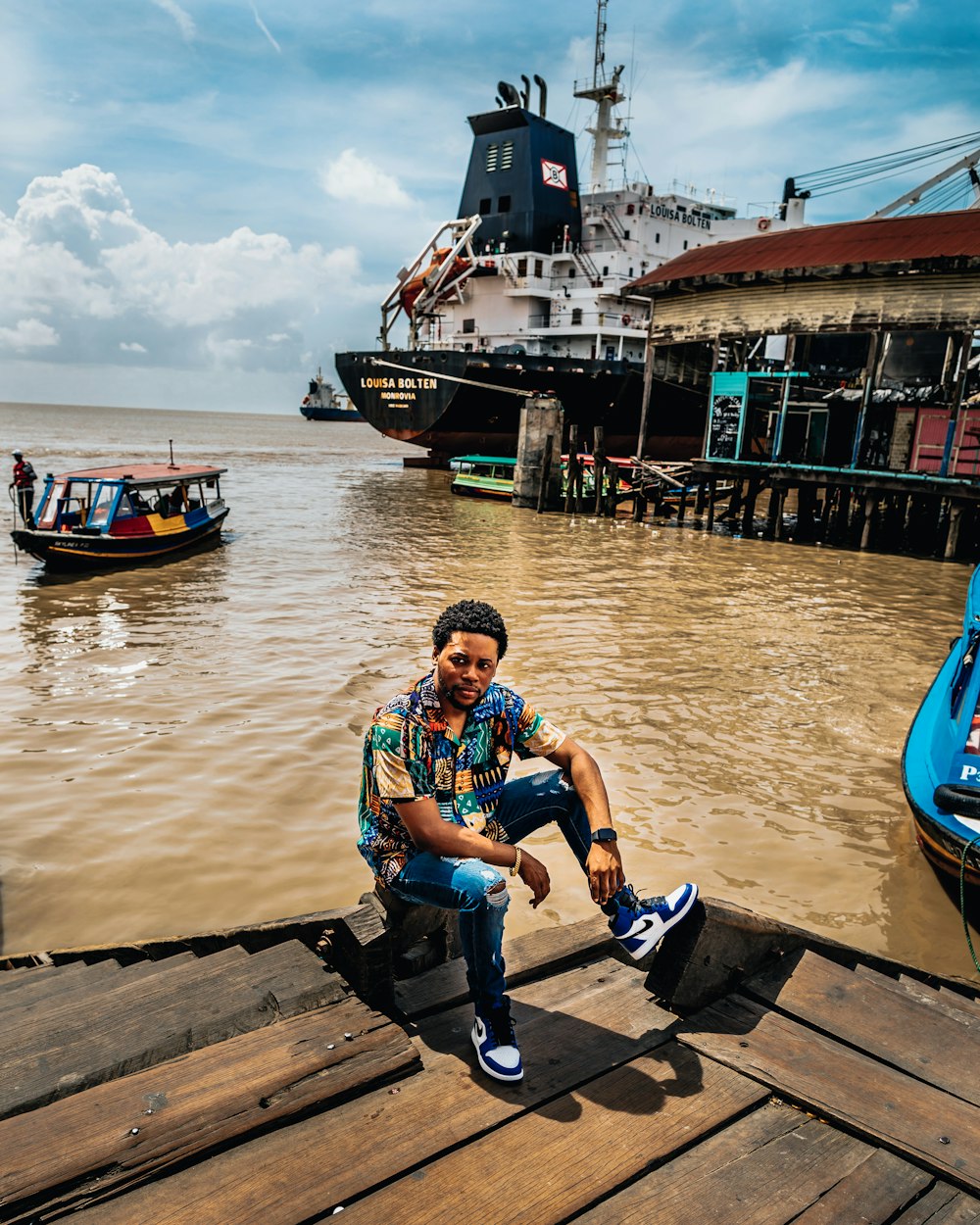 man wearing summer dress shirt sitting on dock near ship and boat