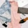 A flat lay arrangement featuring a light denim jacket, a pink dress, a black woven clutch, a coffee cup, a black pointed shoe, a watch, a black smartphone, and a magazine titled 'Collective'. The items are stylishly placed on a white surface, emphasizing a casual yet fashionable theme.