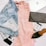 A flat lay arrangement featuring a light denim jacket, a pink dress, a black woven clutch, a coffee cup, a black pointed shoe, a watch, a black smartphone, and a magazine titled 'Collective'. The items are stylishly placed on a white surface, emphasizing a casual yet fashionable theme.
