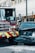 A fire truck and a black Nissan vehicle are involved in a collision at an urban intersection. The front of the car is severely damaged and white powder is visible on the ground, possibly from a fire extinguisher. The surroundings include city buildings and traffic lights.