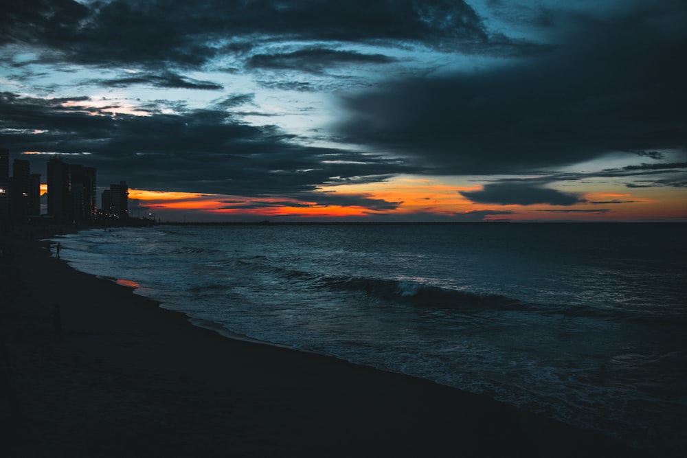 a sunset over the ocean with a city in the distance