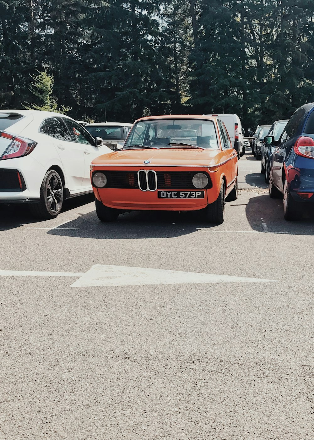 orange vehicle beside white sedan and black vehicle on parking lot