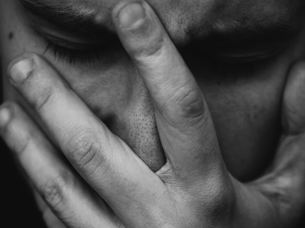 Foto in scala di grigi di persona che mette la mano sul viso