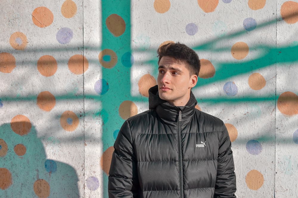 man wearing black zip-up jacket standing beside white and red polka-dot wall