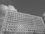A multi-story concrete building with numerous windows is shown with the words 'Hotel Katowice' on the rooftop. The sky is partly cloudy, and there are wires and a pole visible.
