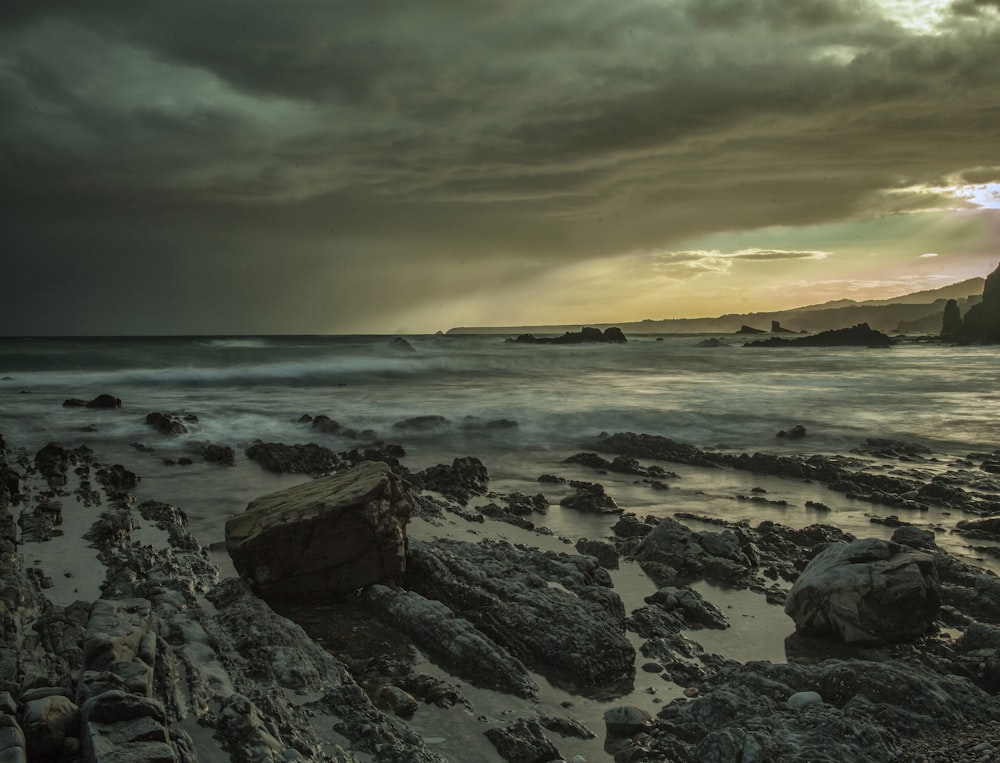 a beach with rocks and water under a cloudy sky