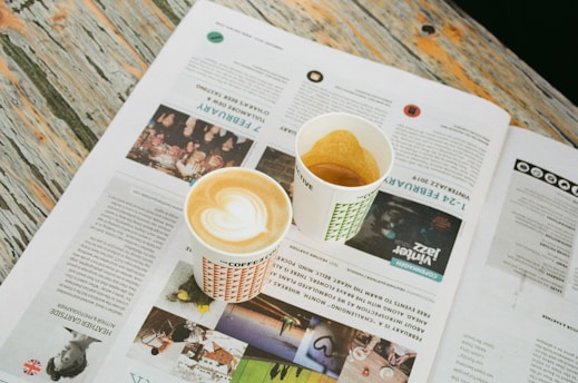 Um copo de café capuccino com uma imagem de coração repousa sobre a página de uma revista