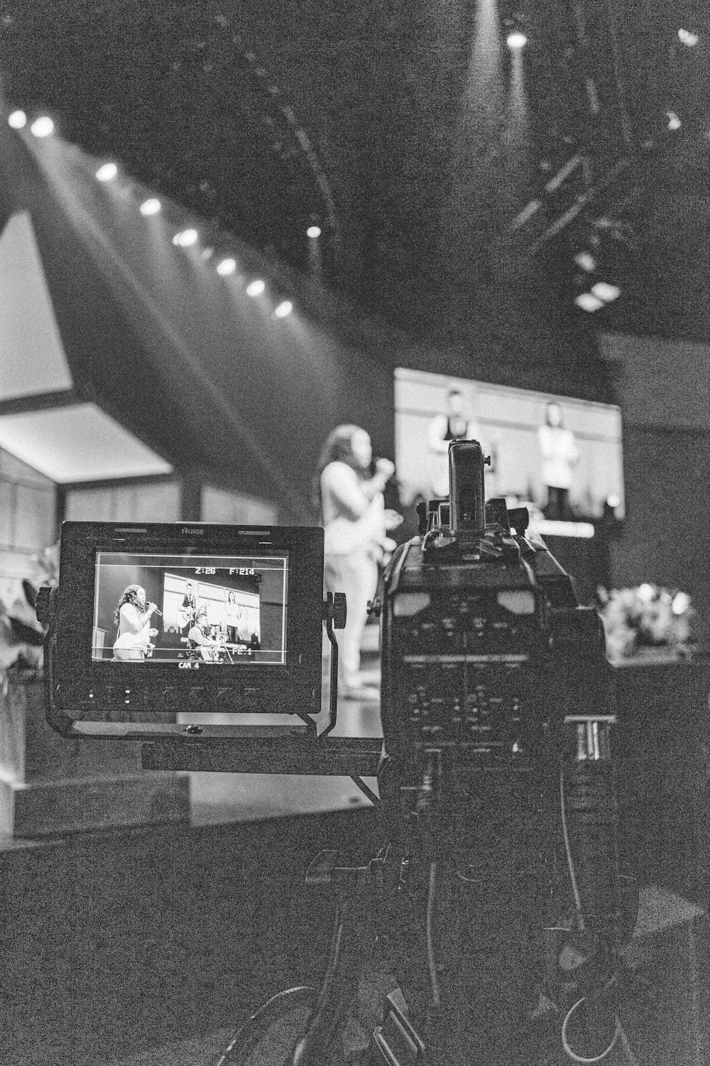 greyscale photography of video camera capturing person standing on stage