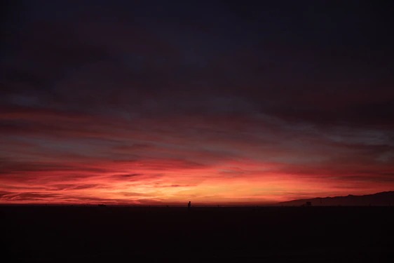 A rugged yet refined landscape at dusk, with a lone cowboy silhouette overlooking vast open land under a deep forest green sky.