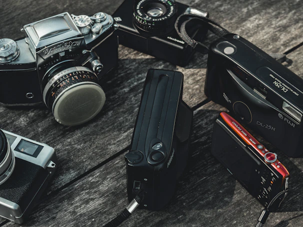 Close-up of hands arranging vintage film cameras on a textured wooden table.