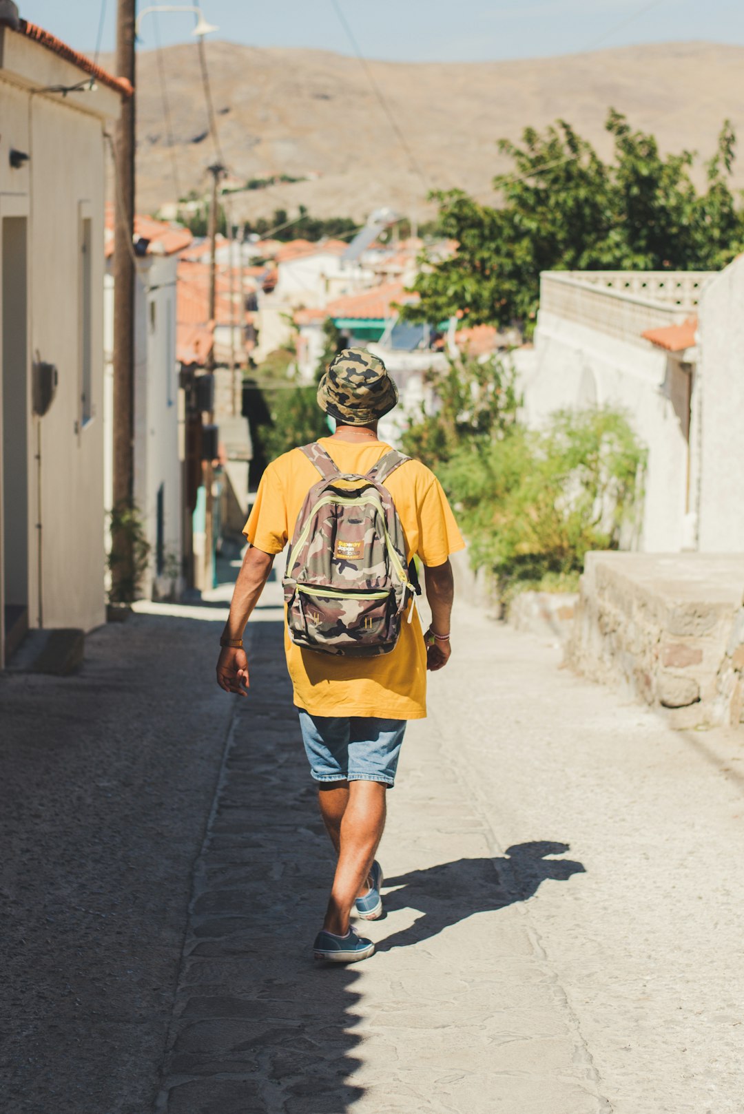 person wearing brown shirt walking on street while carrying backpack