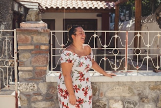 A candid shot of a woman laughing outdoors, wearing a flowing white dress against a muted background.