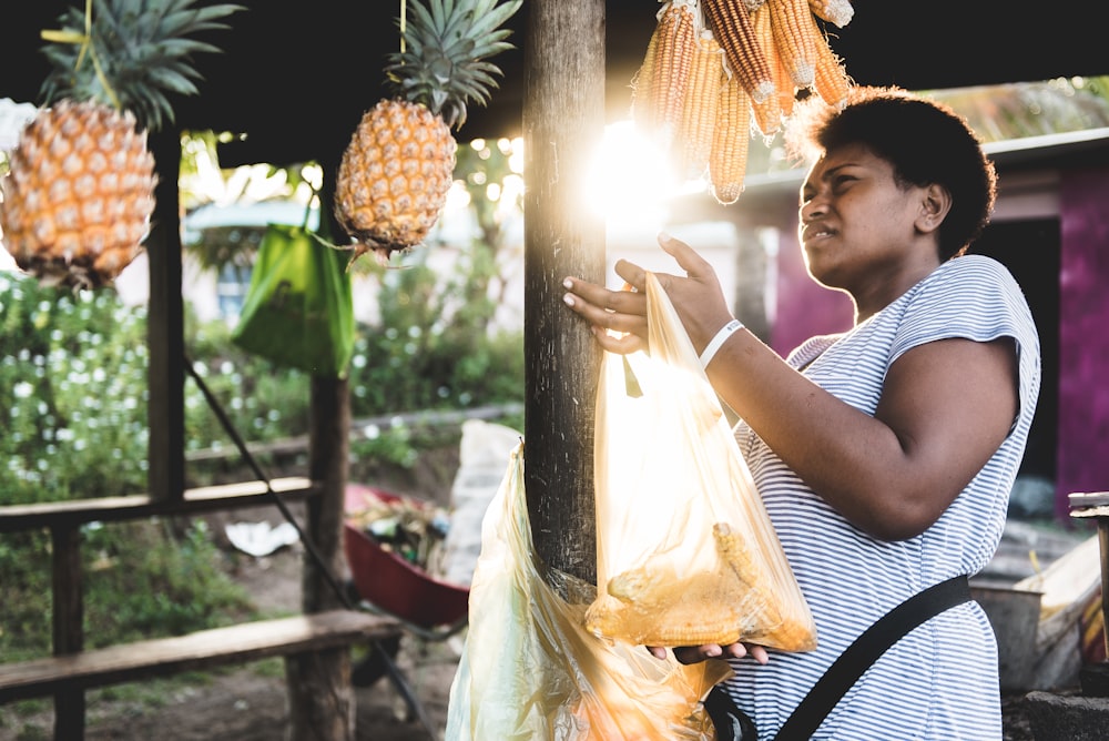 Mulher segurando saco plástico amarelo perto de frutas do abacaxi