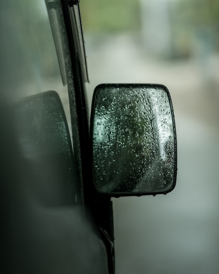 A close-up of a sensor device with raindrops and fog in the background, illustrating weather impact.
