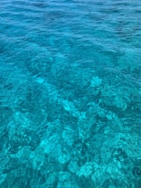 The image features clear turquoise water with visible patterns created by sunlight reflecting on the surface. The water appears calm and inviting, showcasing varying shades of blue and green.
