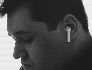 A close-up black and white profile of a person wearing wireless earphones. The person appears to be introspective, with eyes closed and a calm expression.