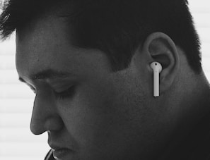 A close-up black and white profile of a person wearing wireless earphones. The person appears to be introspective, with eyes closed and a calm expression.