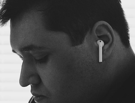 A close-up black and white profile of a person wearing wireless earphones. The person appears to be introspective, with eyes closed and a calm expression.