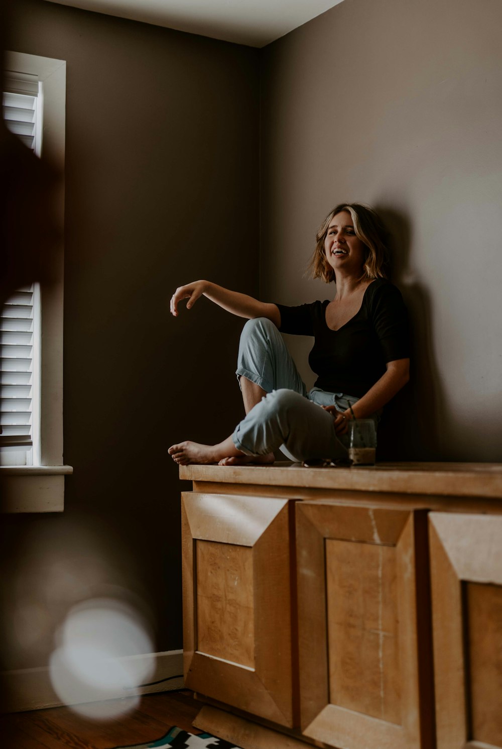 woman sitting on wooden sideboard against wall