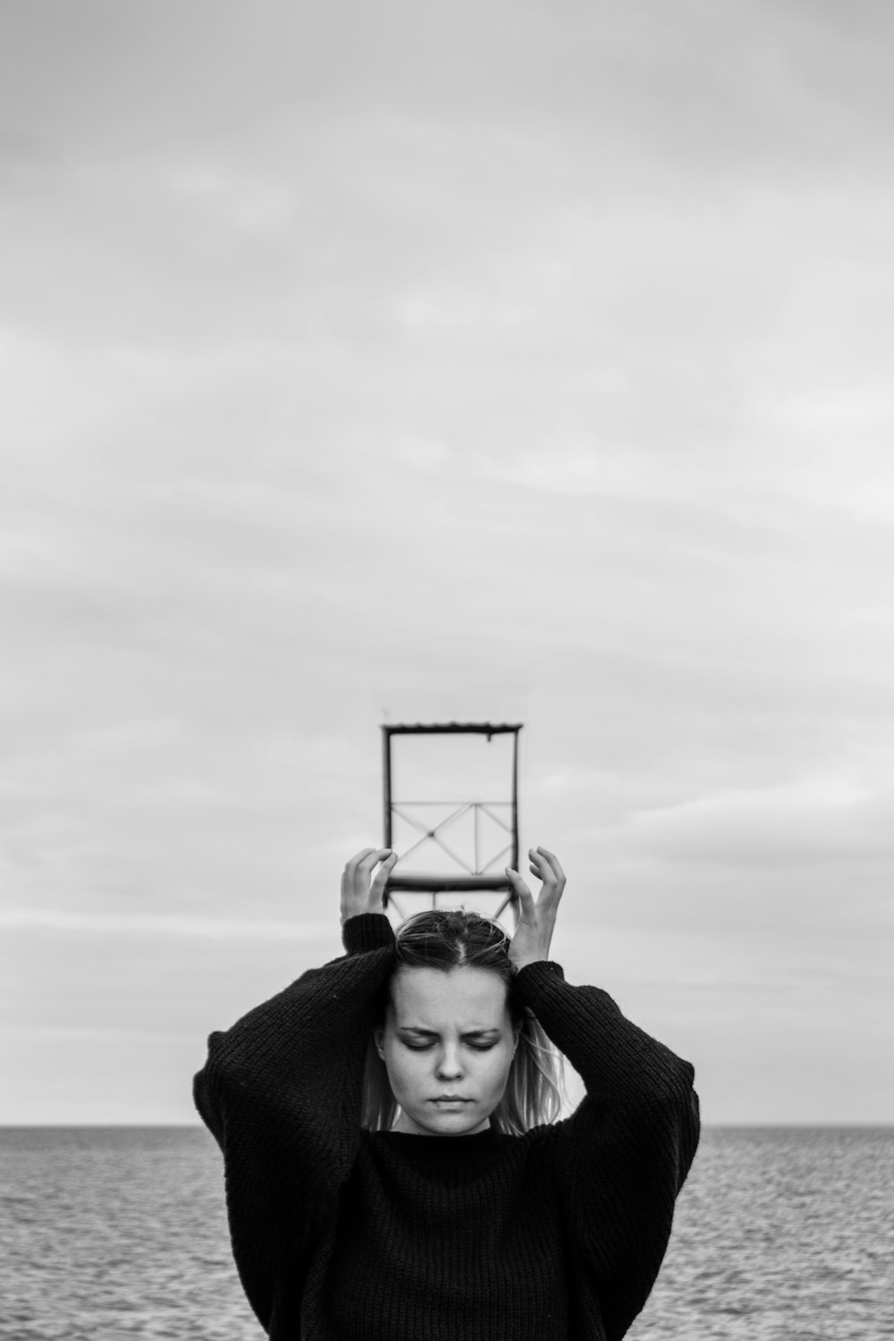 fotografia in scala di grigi di donna che tiene una cornice metallica quadrata sopra la testa