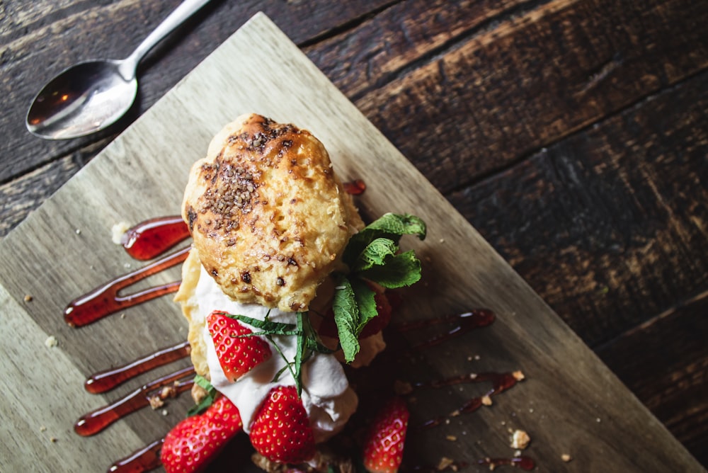 bollos a la parrilla sobre crema blanca, fresas en rodajas y verduras de hoja verde rociadas con salsa roja