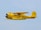 A vintage yellow aircraft is flying against a clear blue sky. It features a distinctive radial engine and a streamlined fuselage with black and red accents. The registration number N9405H is visible on the tail.