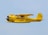 A vintage yellow aircraft is flying against a clear blue sky. It features a distinctive radial engine and a streamlined fuselage with black and red accents. The registration number N9405H is visible on the tail.