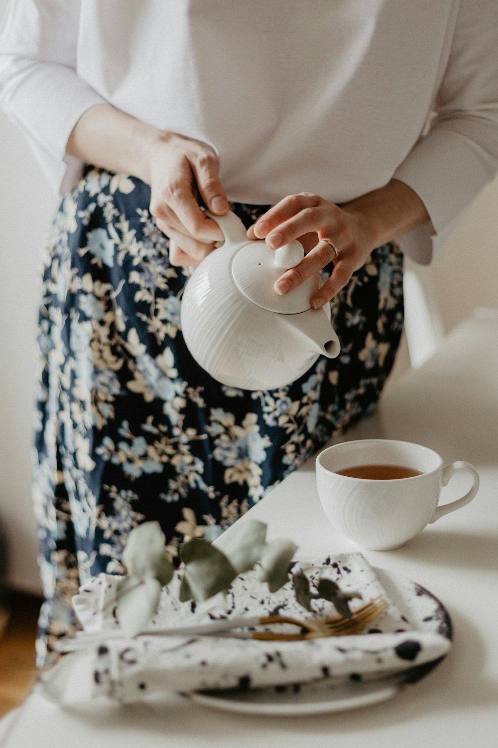 Frau mit Teekanne, die auf Kaffeetasse auf Tisch gießt